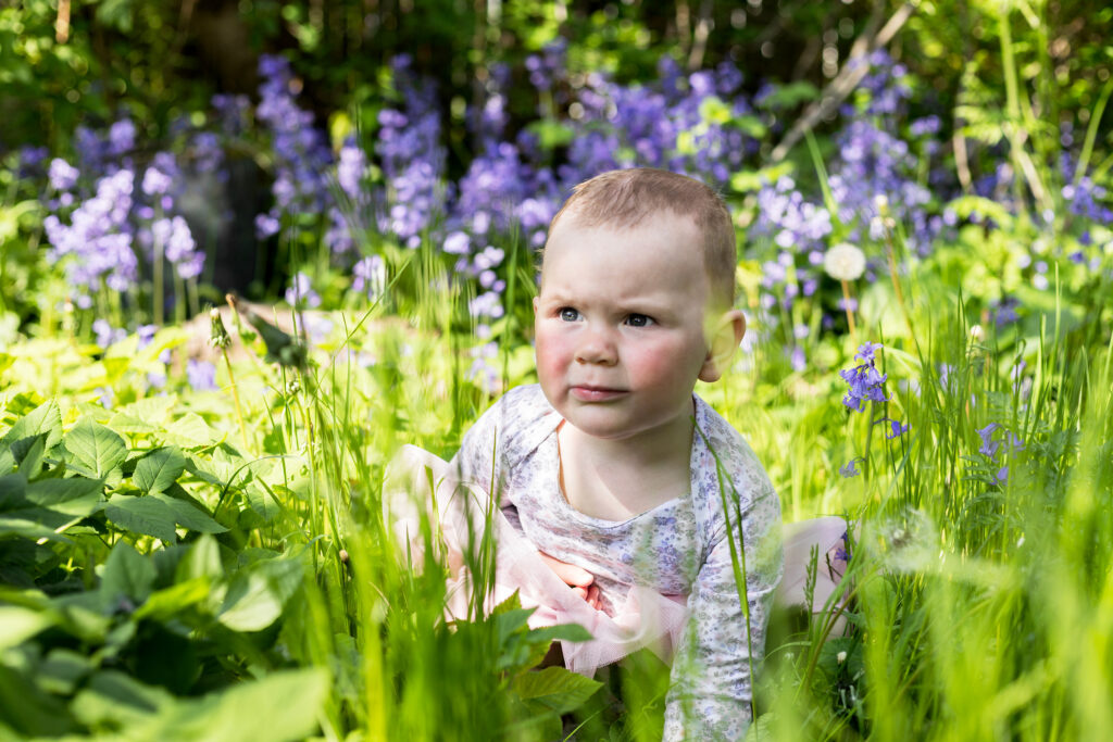 Portræt af en lille pige på 18 måneder ude i naturen omgivet af blomster