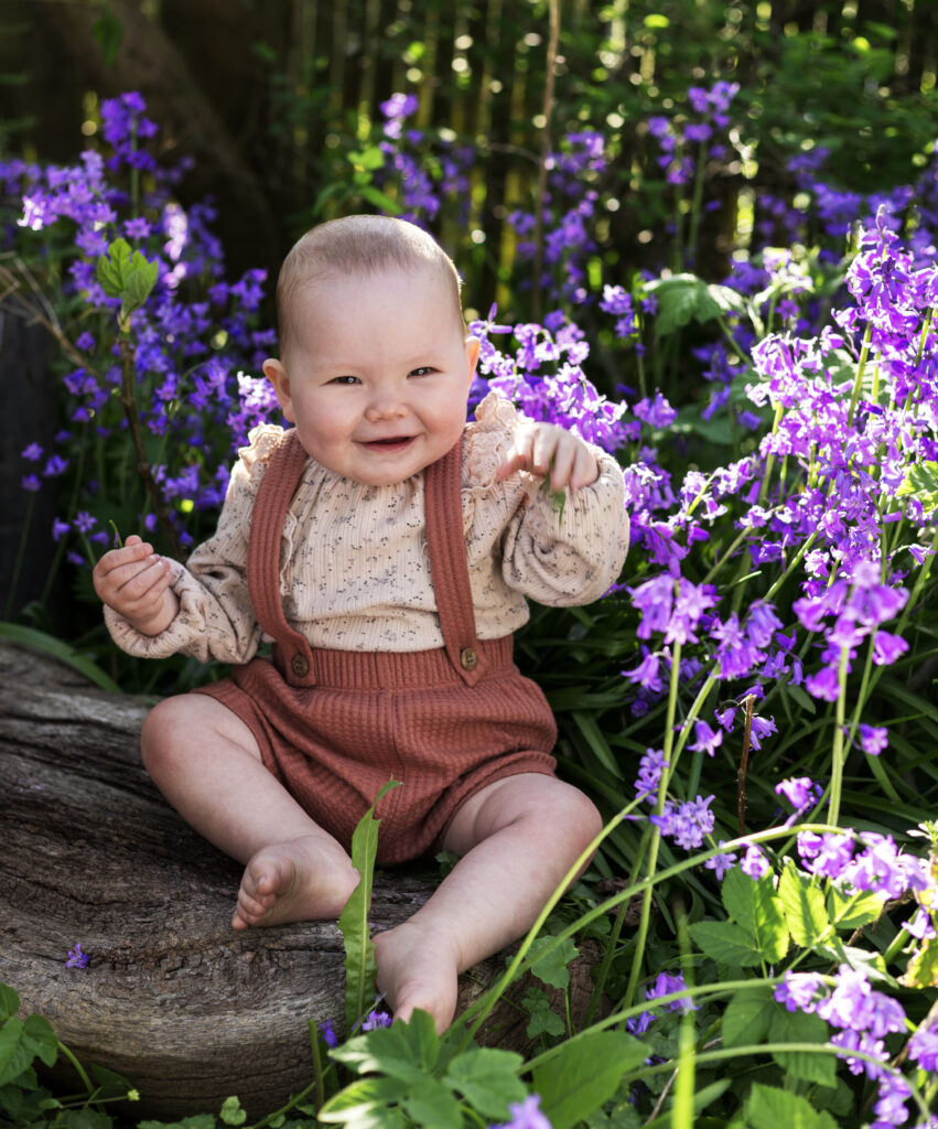 Portrætfoto af en 10 måneder gammel pige ude i naturen blandt blomster